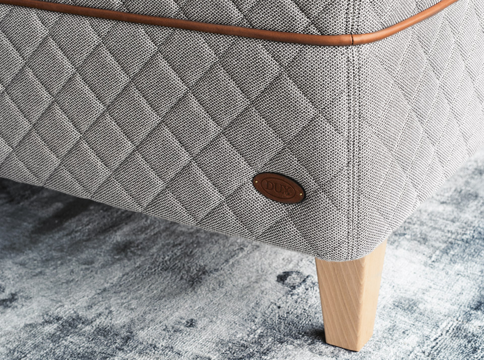 Detail of the DUX 3003 bed and tapered bed legs on a light green carpet. 